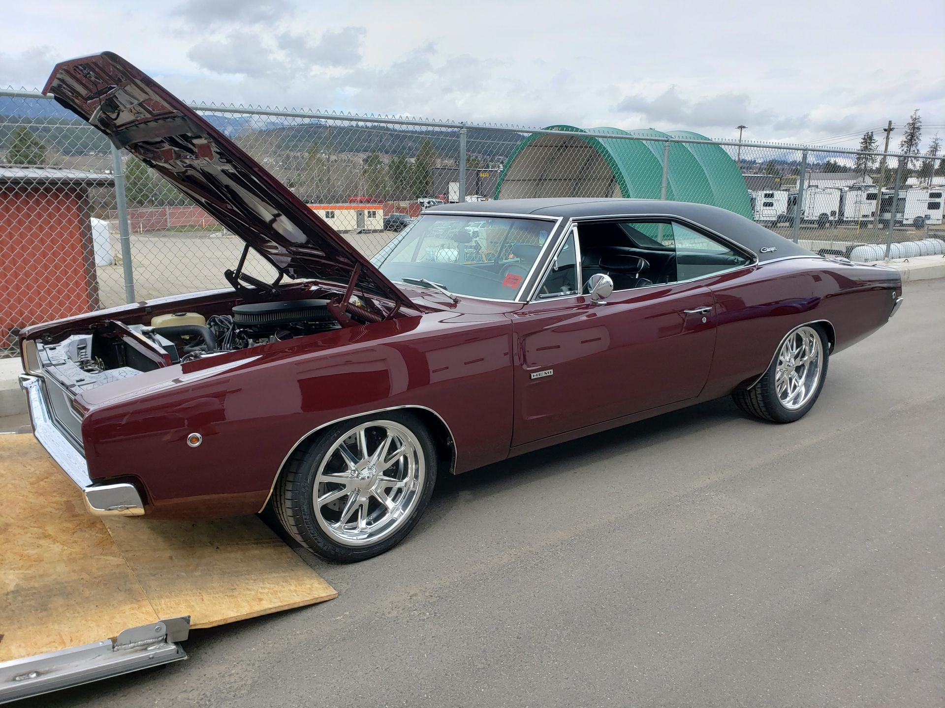 A burgundy dodge charger with the hood up is parked in a parking lot.