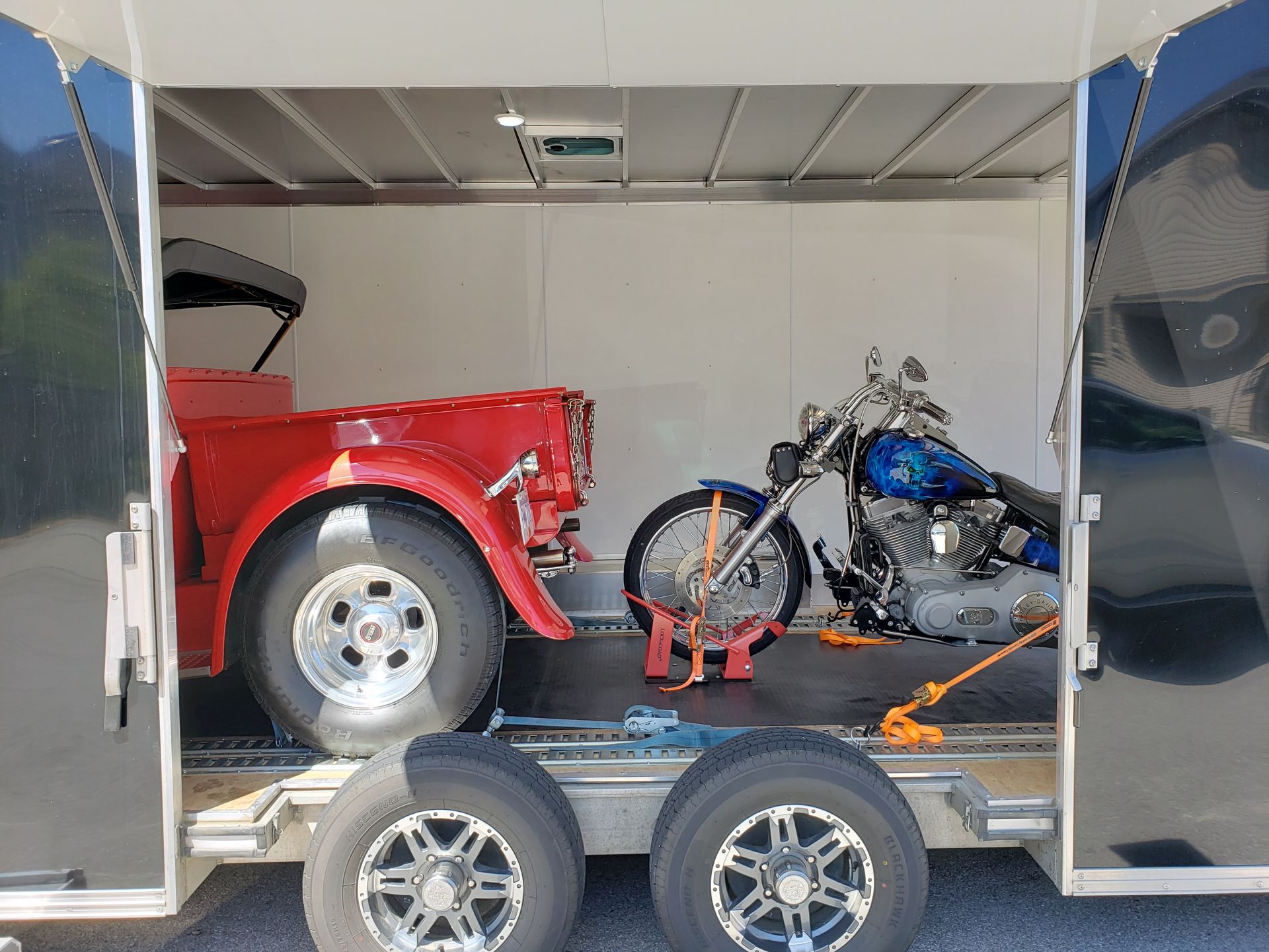 A red truck and a motorcycle are in a trailer.