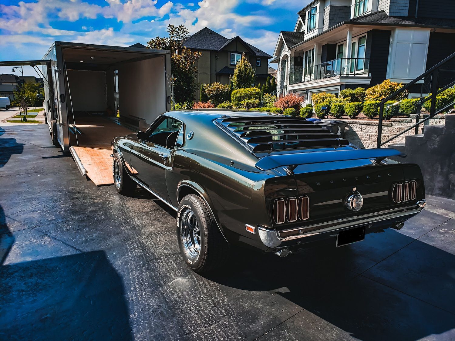 A black mustang is parked in a driveway next to a trailer.
