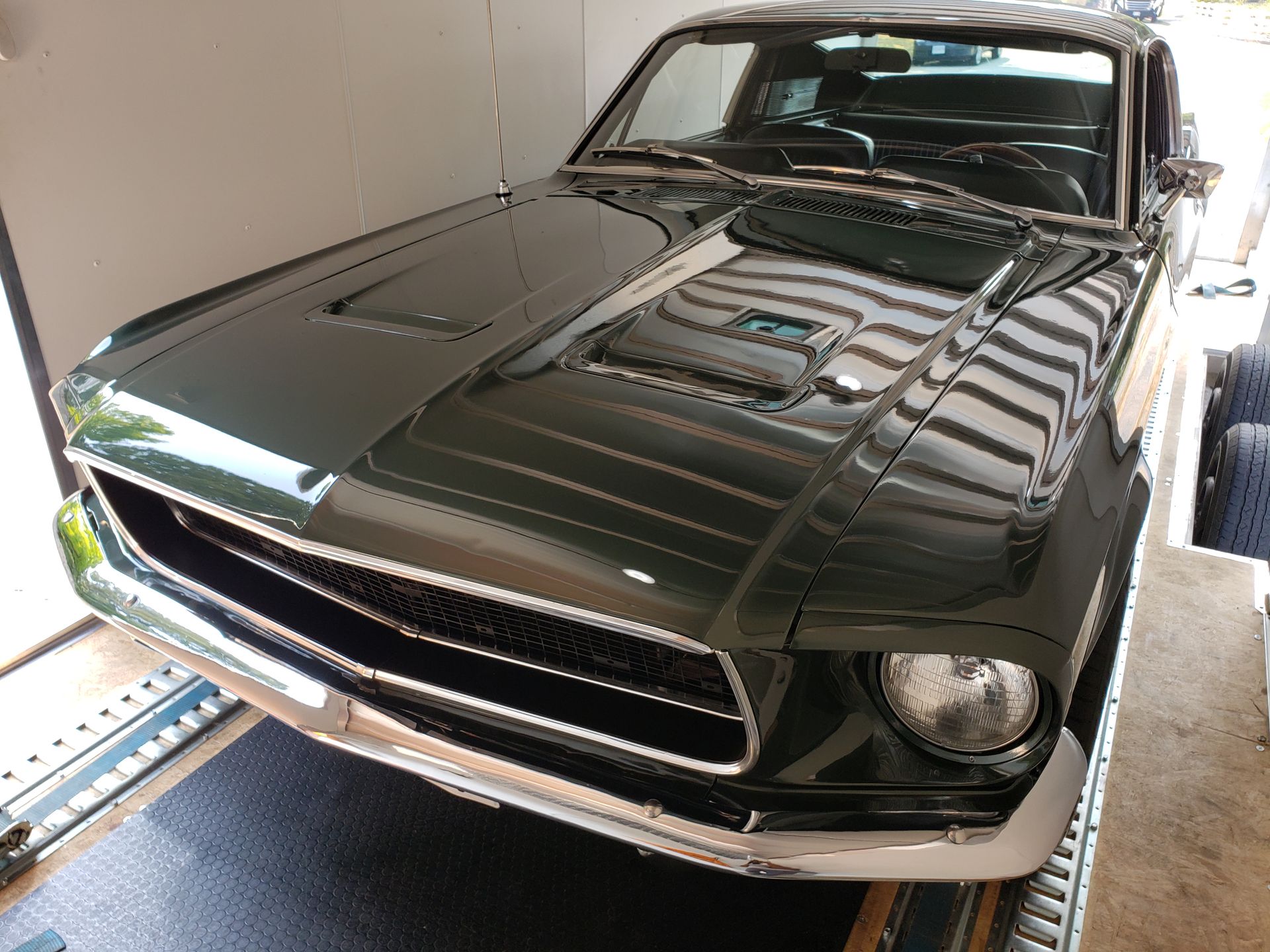 A green mustang is parked on a trailer in a garage