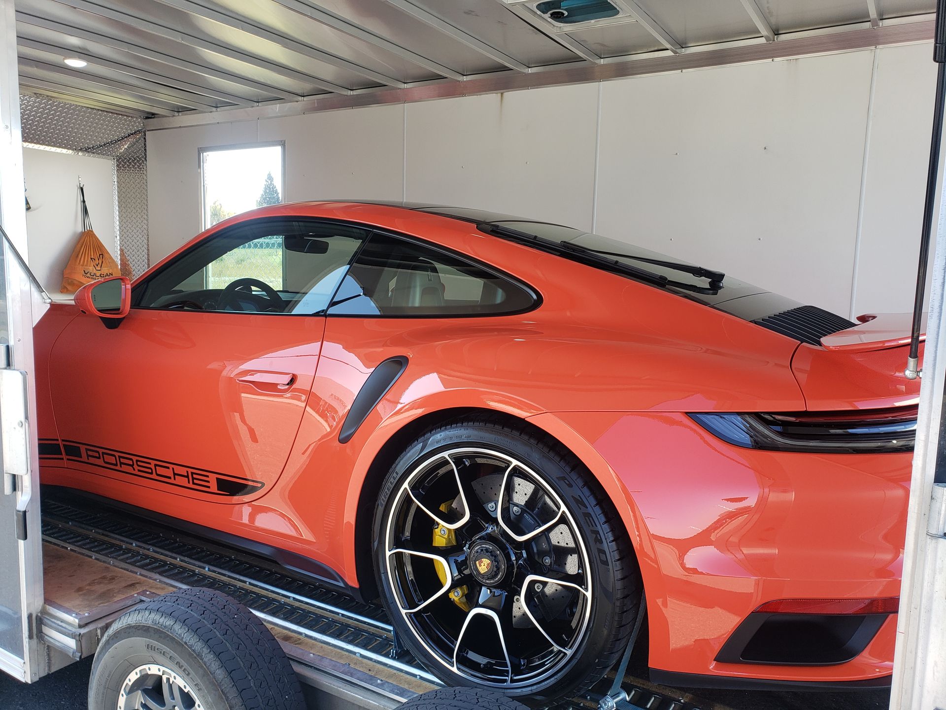 An orange porsche 911 turbo s is being towed by a trailer.