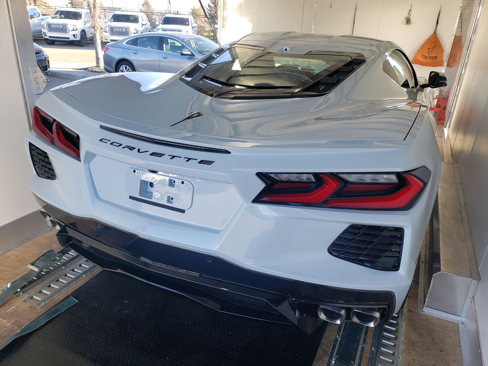 A white corvette is parked in a garage on a trailer.