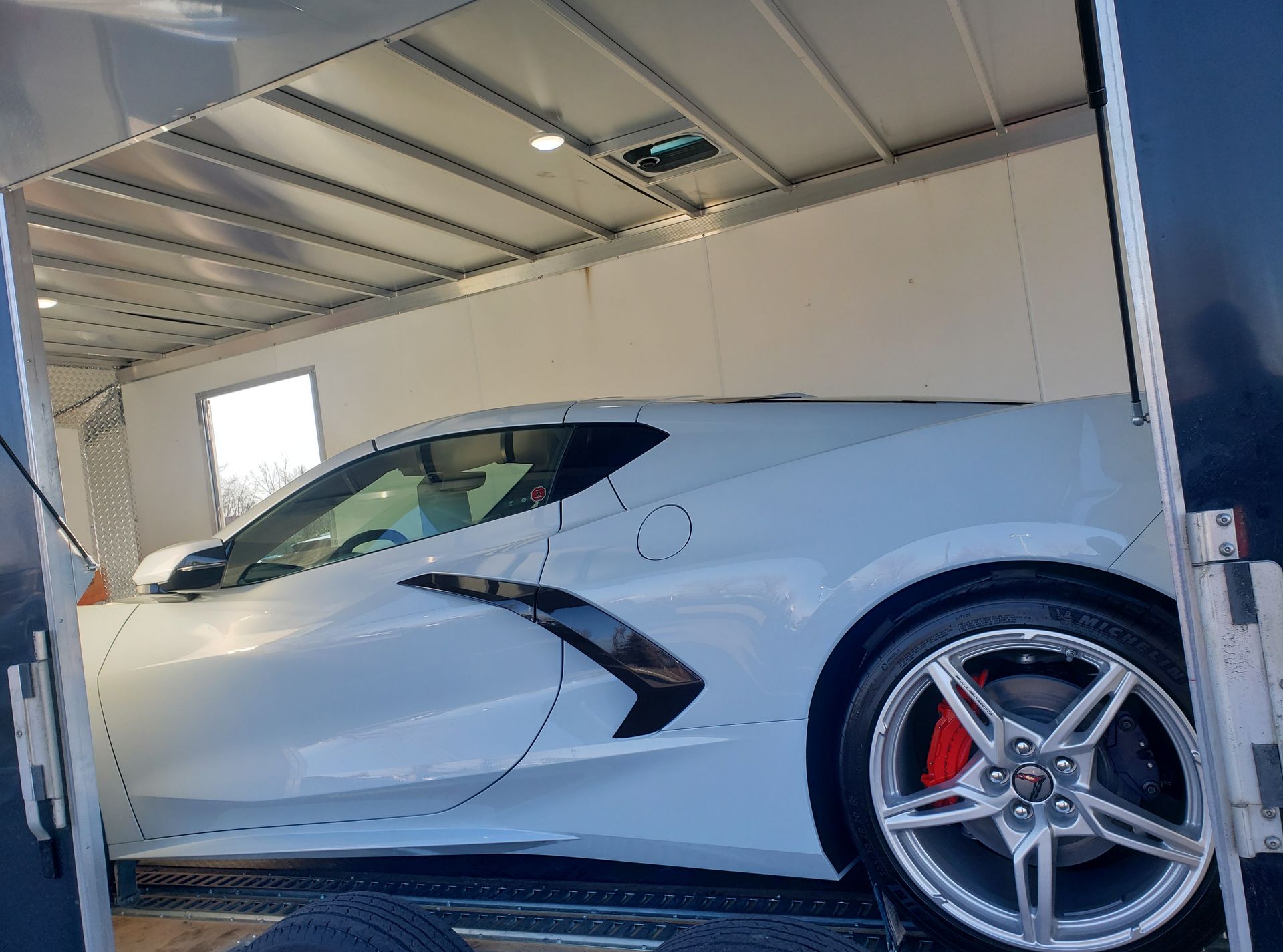 A white sports car is sitting inside of a trailer.
