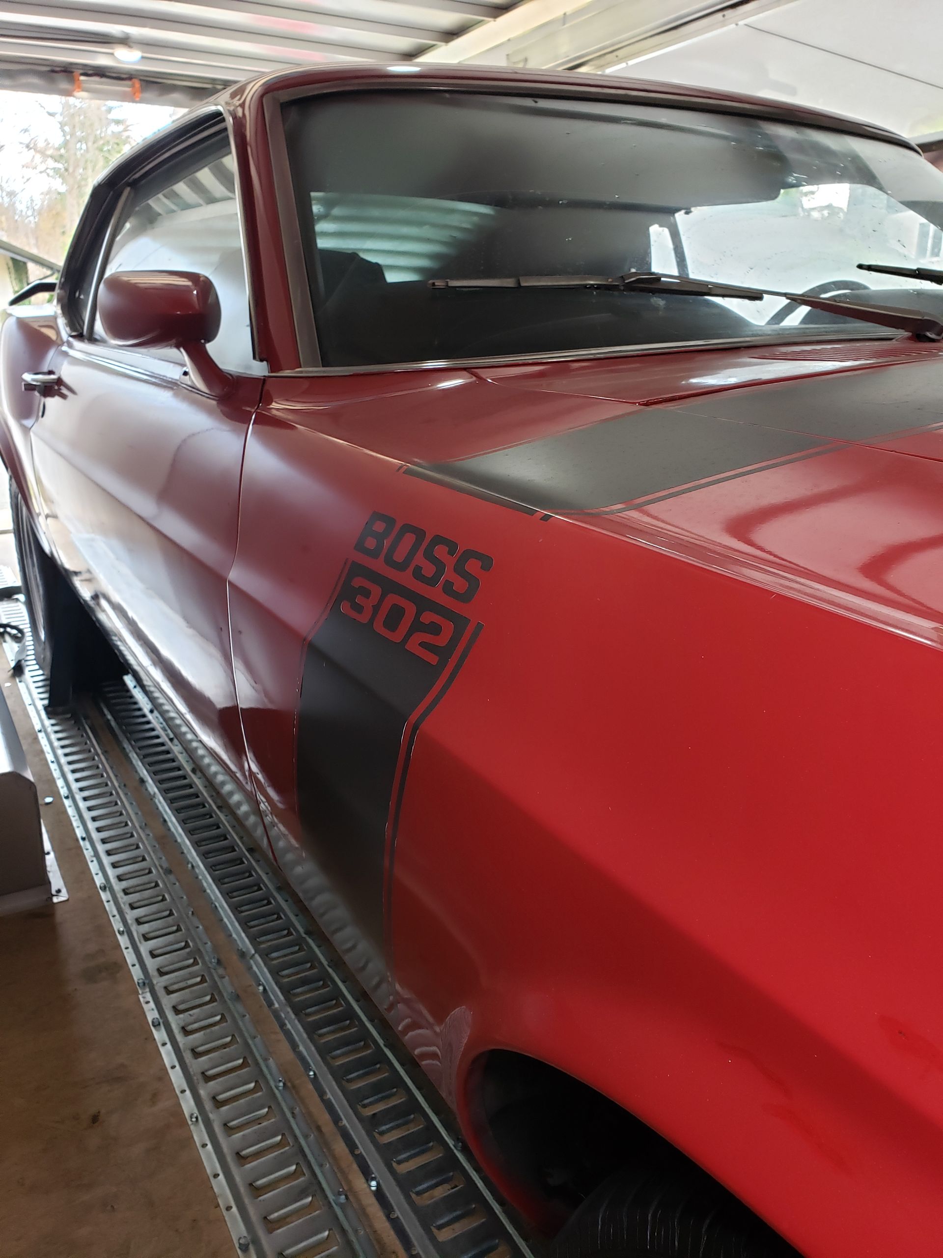 A red mustang boss 302 is parked in a garage