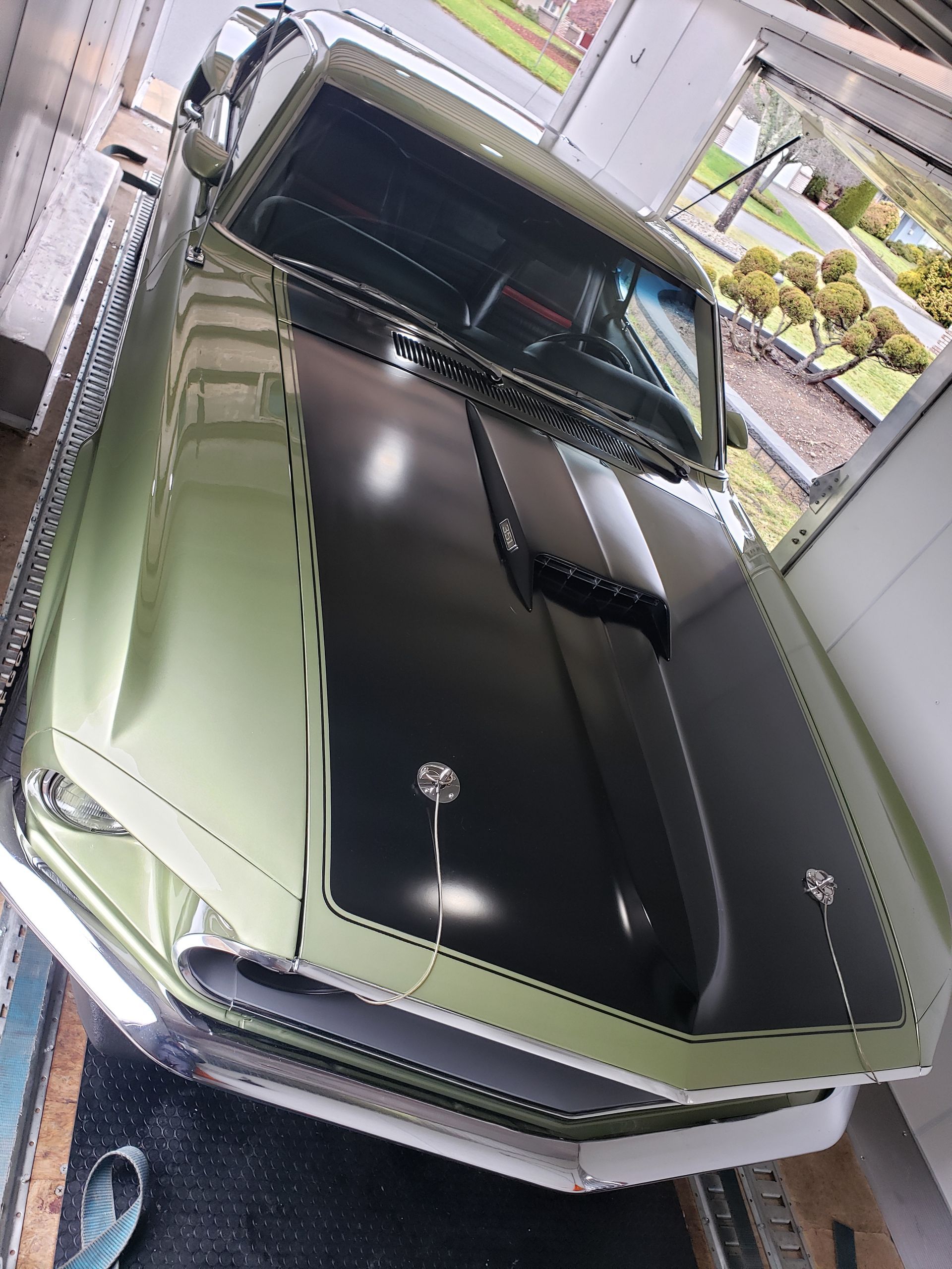 A green car with a black hood is parked in a garage