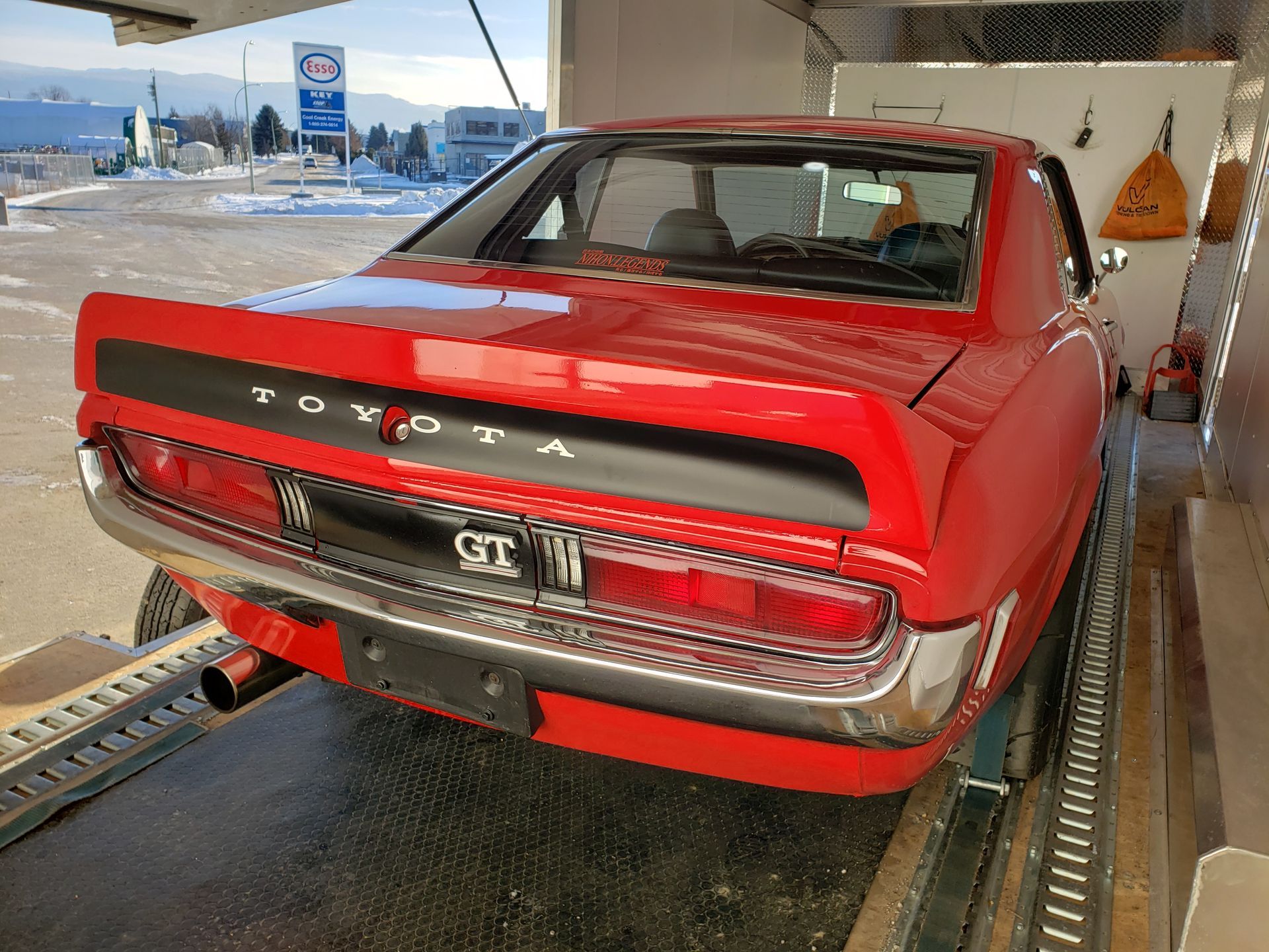 A red toyota gt is sitting on a trailer in a parking lot.