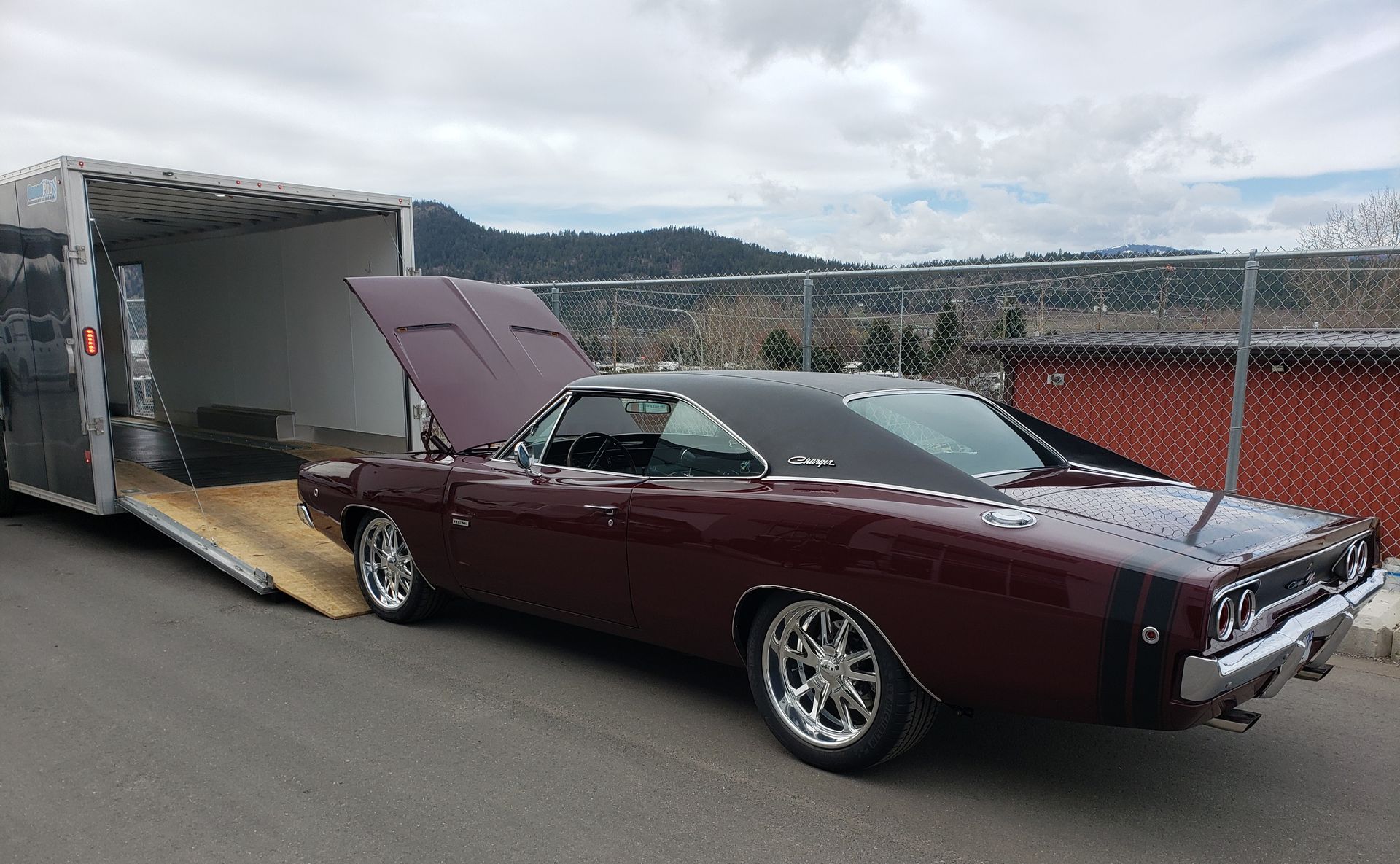 A purple dodge charger is parked in front of a trailer.