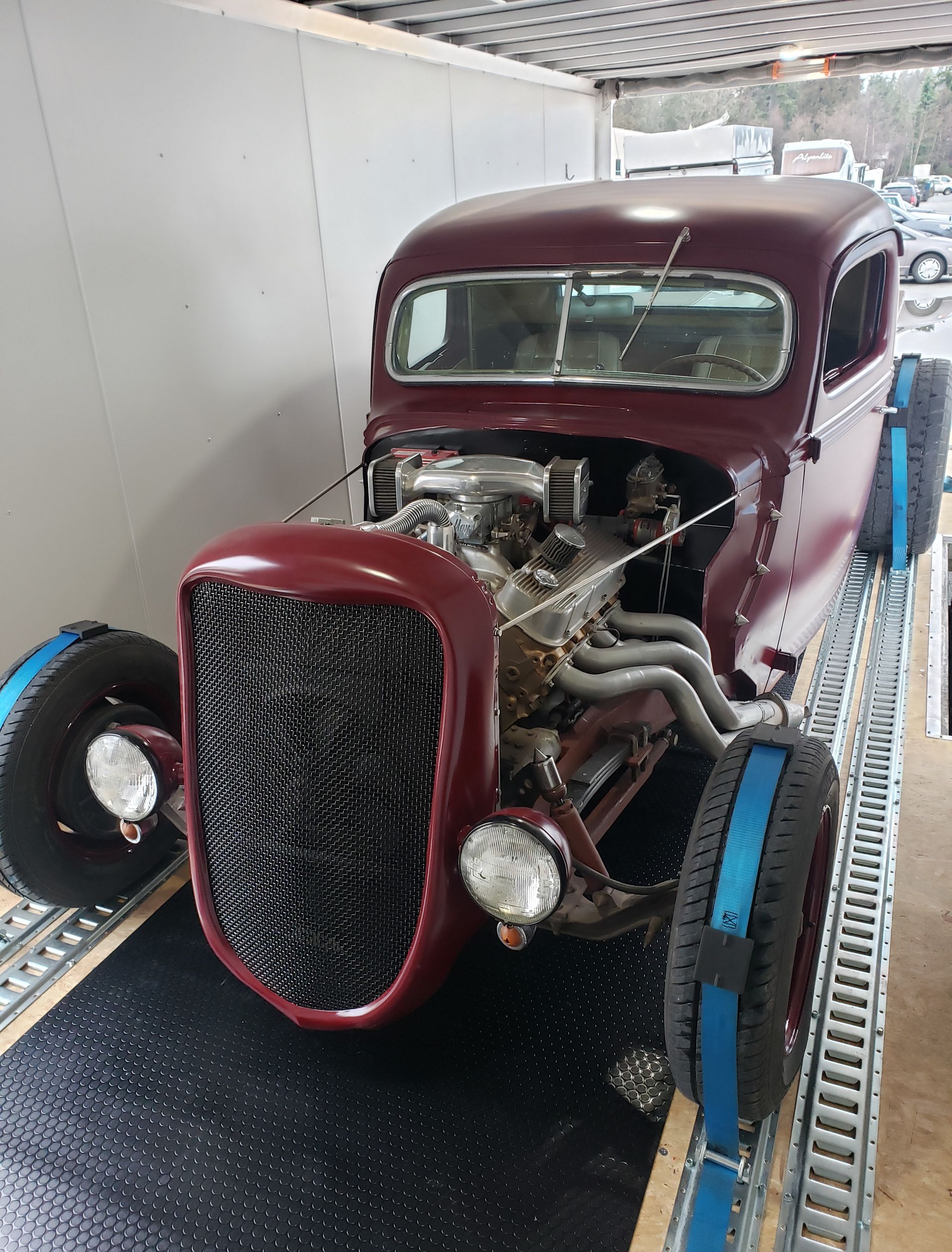 A red car is sitting on a trailer in a garage.