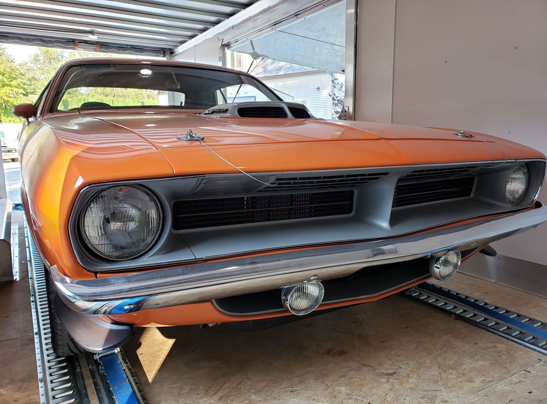 An orange dodge barracuda is parked in a garage.