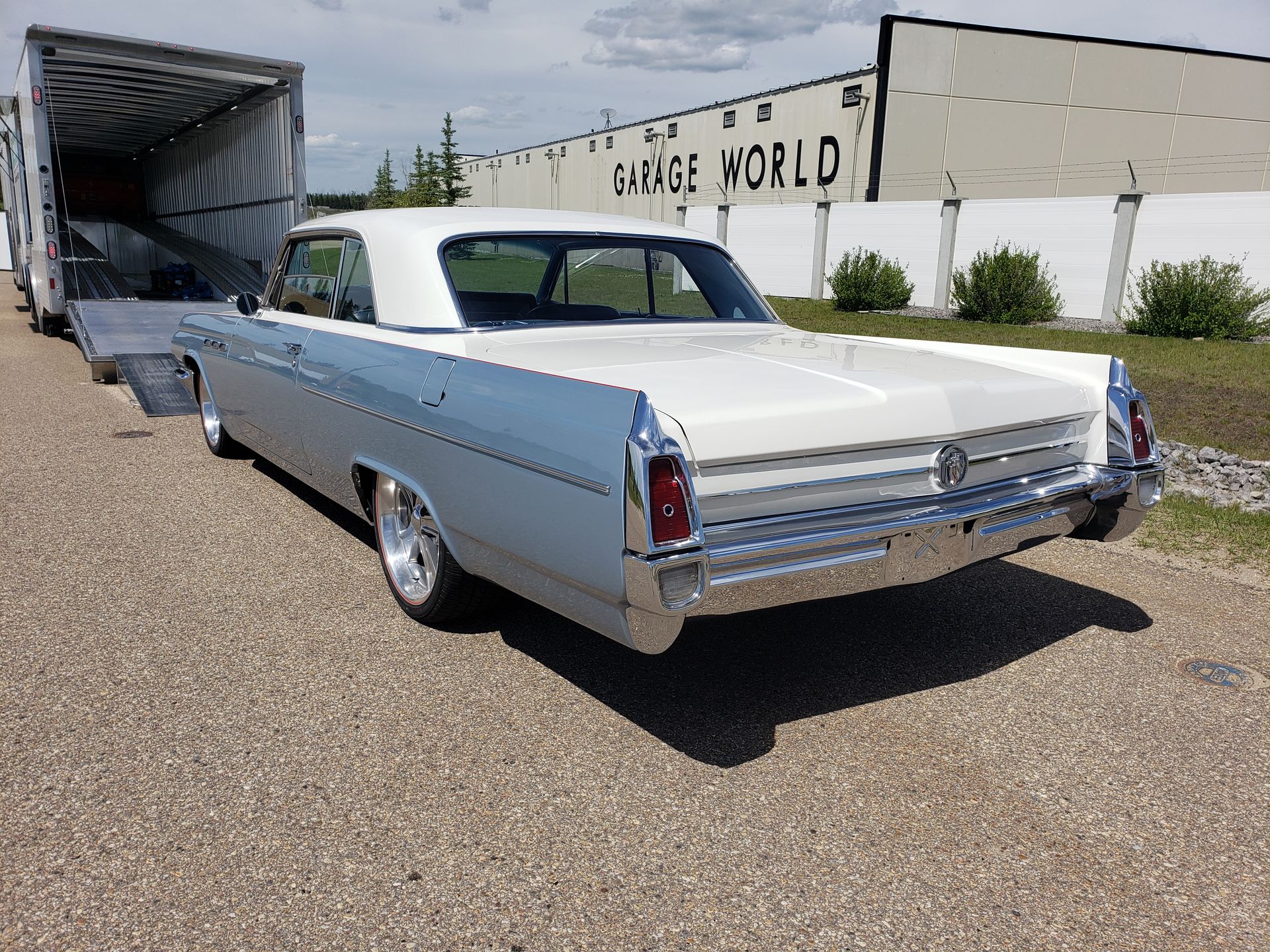 A silver and white car is parked in front of a garage world building.