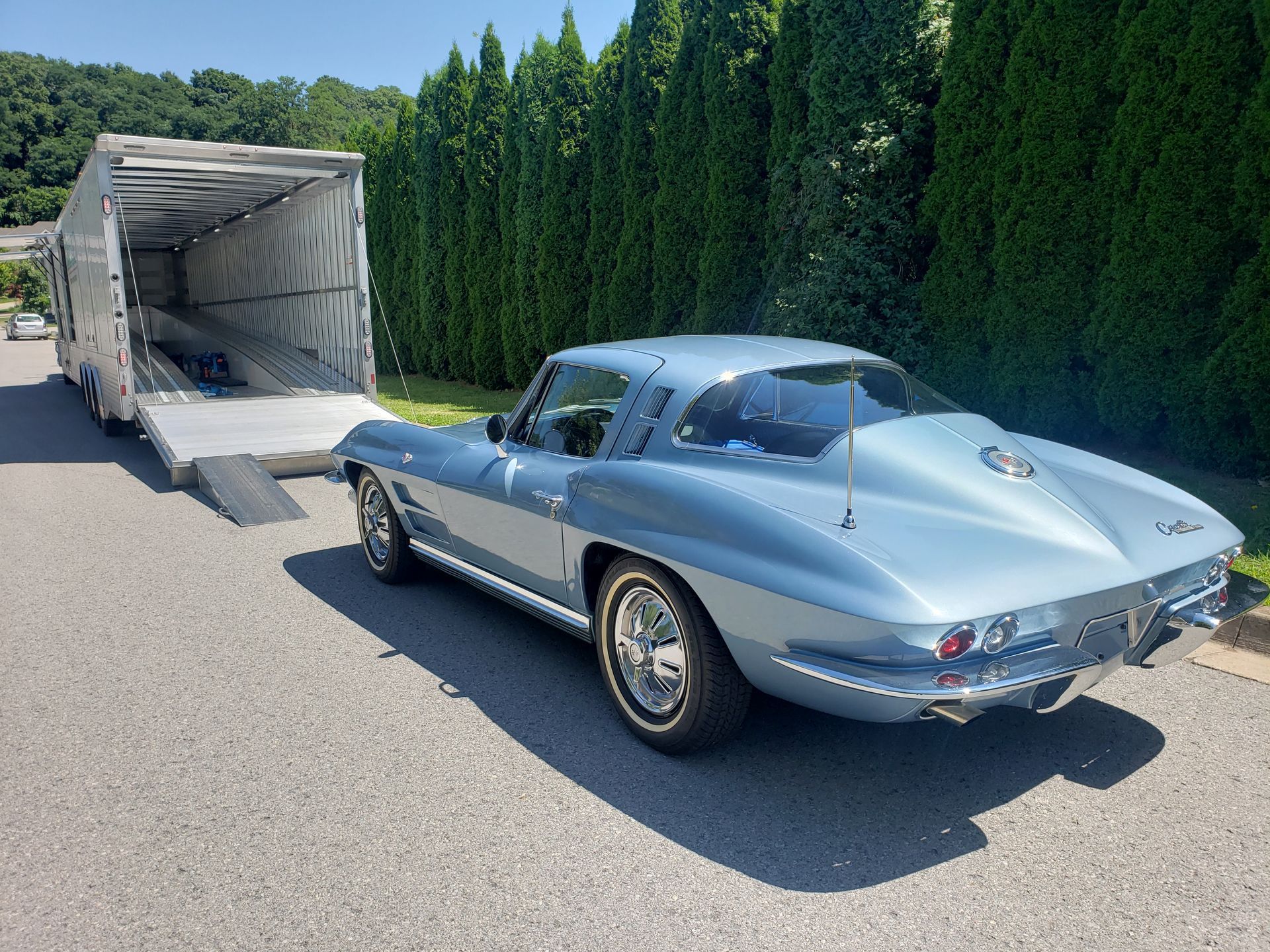 A blue corvette is parked next to a trailer.