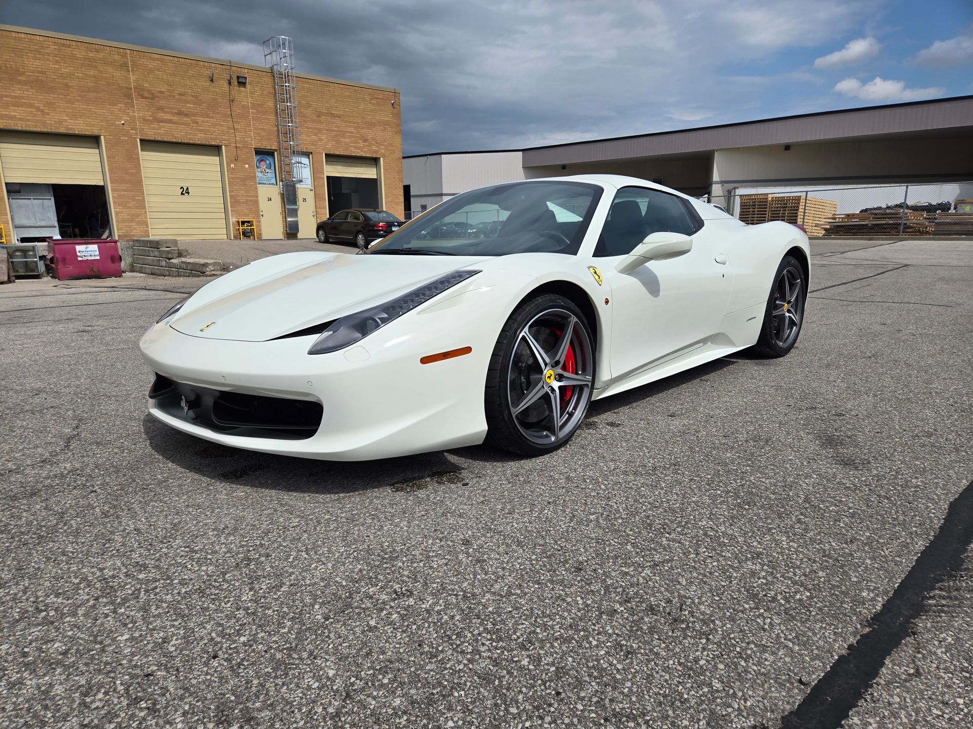 A white ferrari 458 italia is parked in a parking lot in front of a building.