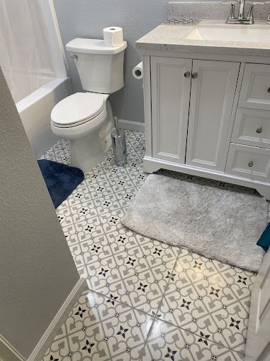 Bathroom with patterned tile floor, white vanity, toilet, and bath mat.