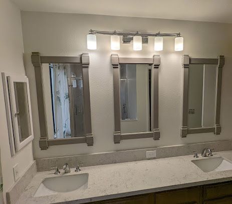 Bathroom with three mirrors, vanity, and overhead lighting. The color scheme is neutral, with wood-framed mirrors.
