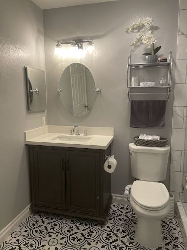Bathroom with dark vanity, patterned tile floor, oval mirror, and silver shelving with towels and decorative items.
