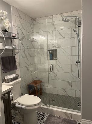 Modern bathroom with white tiled shower, glass door, and toilet.