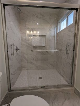 A modern shower with clear glass doors and marble-look tile walls.