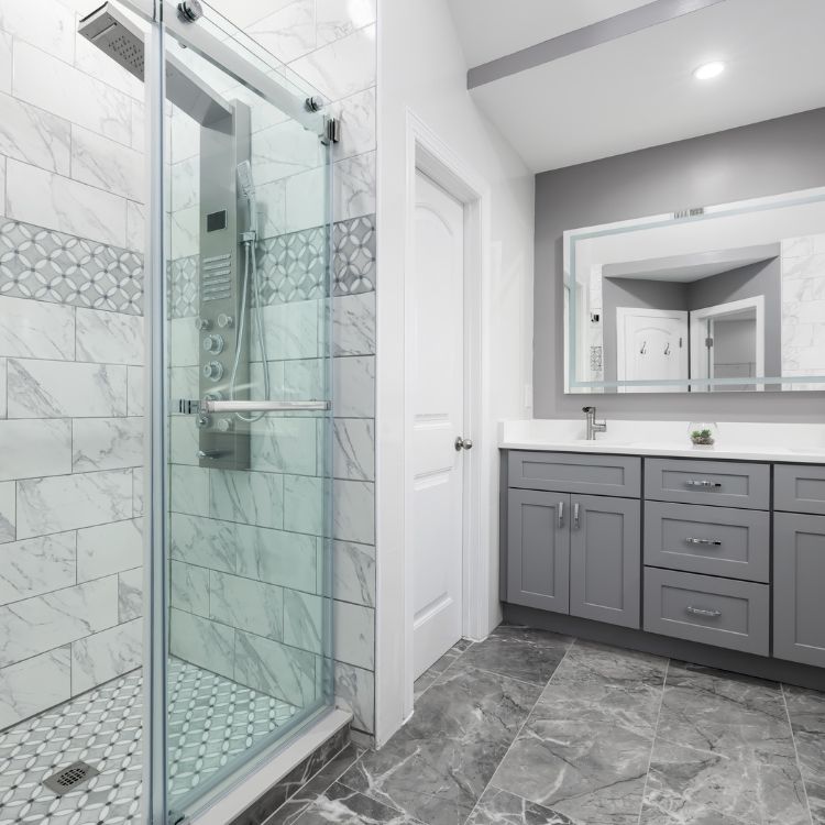 Modern bathroom with gray cabinets, marble-like tiles, a glass shower, and a large mirror.