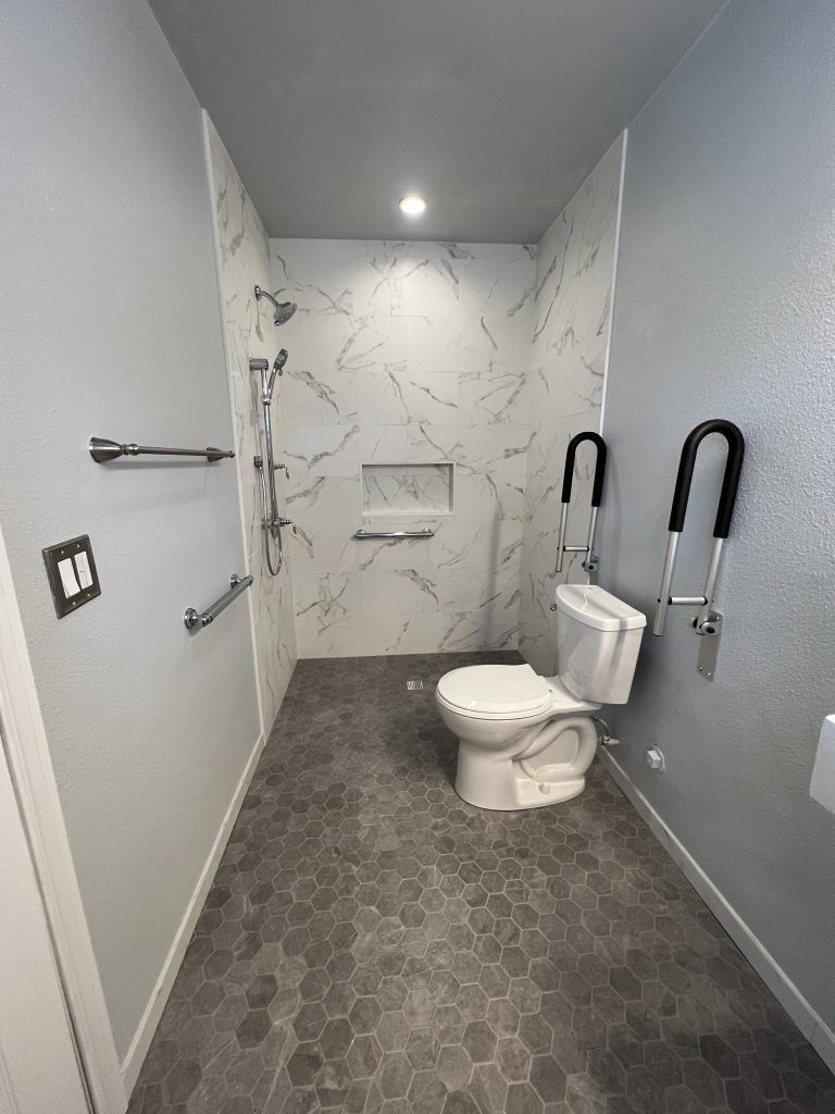 Accessible bathroom with marble tile shower, gray hexagonal floor tiles, and grab bars.