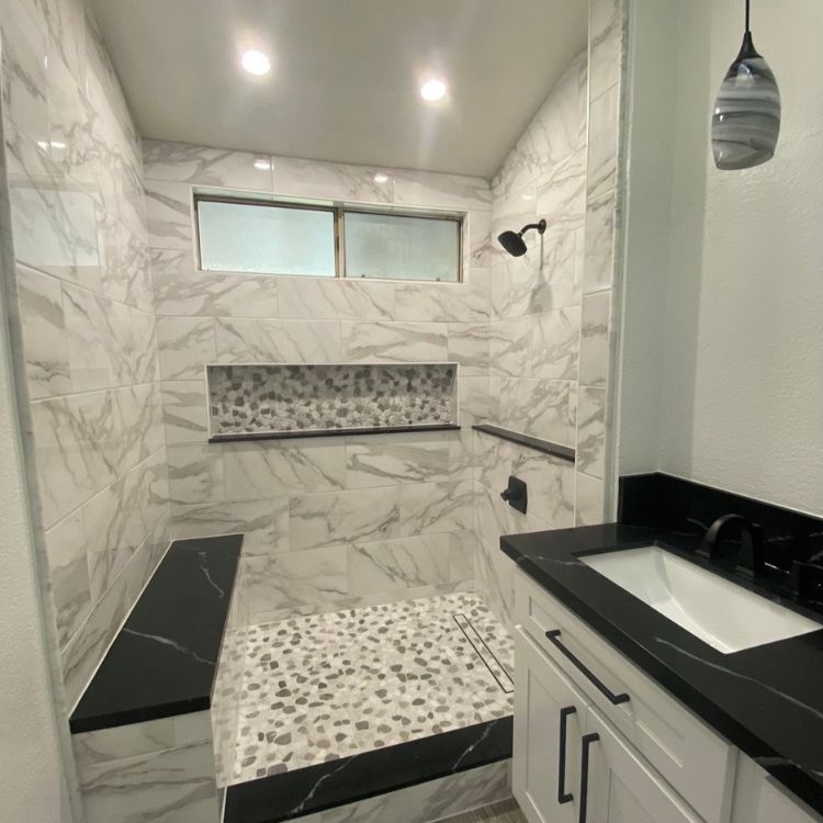 Modern bathroom with marble tile shower, black vanity with white sink, and built-in bench.