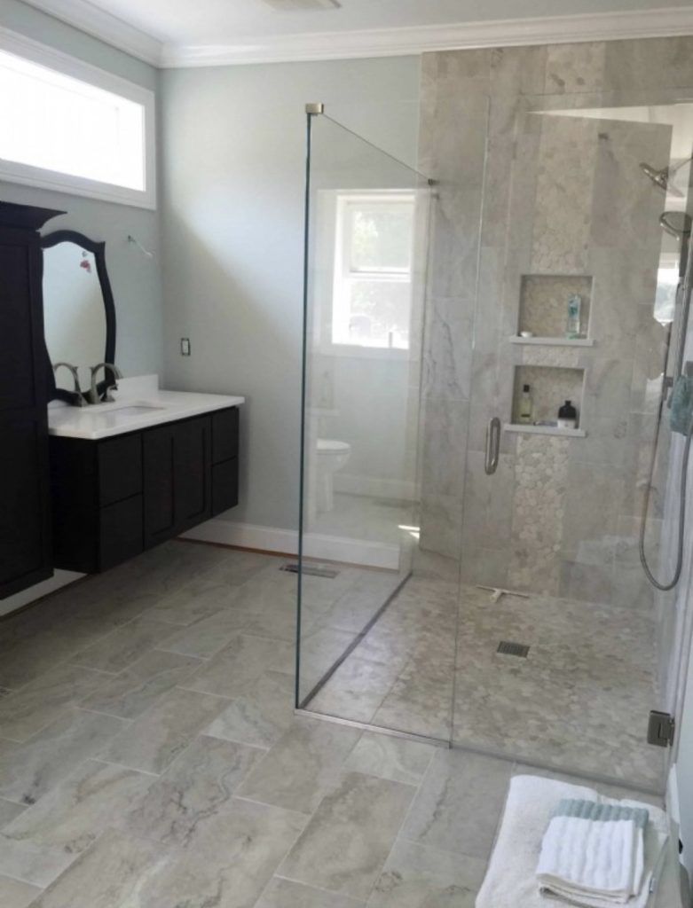 Modern bathroom with glass shower, marble tile, floating vanity, and dark cabinet.
