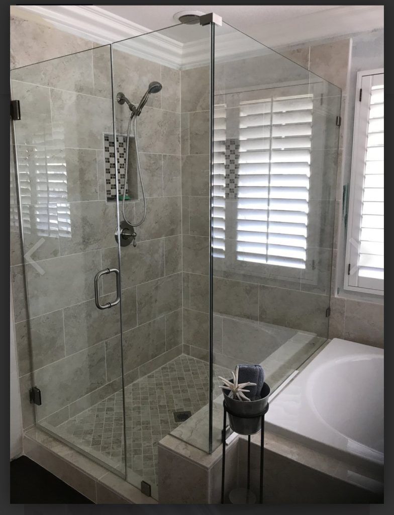 Glass shower enclosure with tiled walls and a bathtub visible.