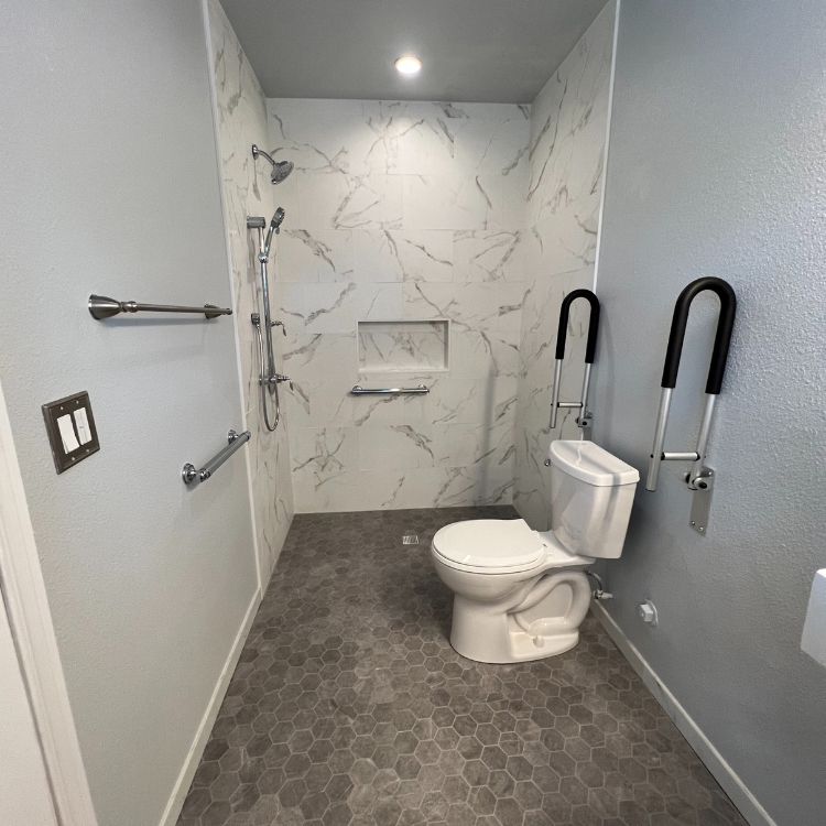 Accessible bathroom with marble tile shower, grab bars, and raised toilet. Gray hexagon tile floor.