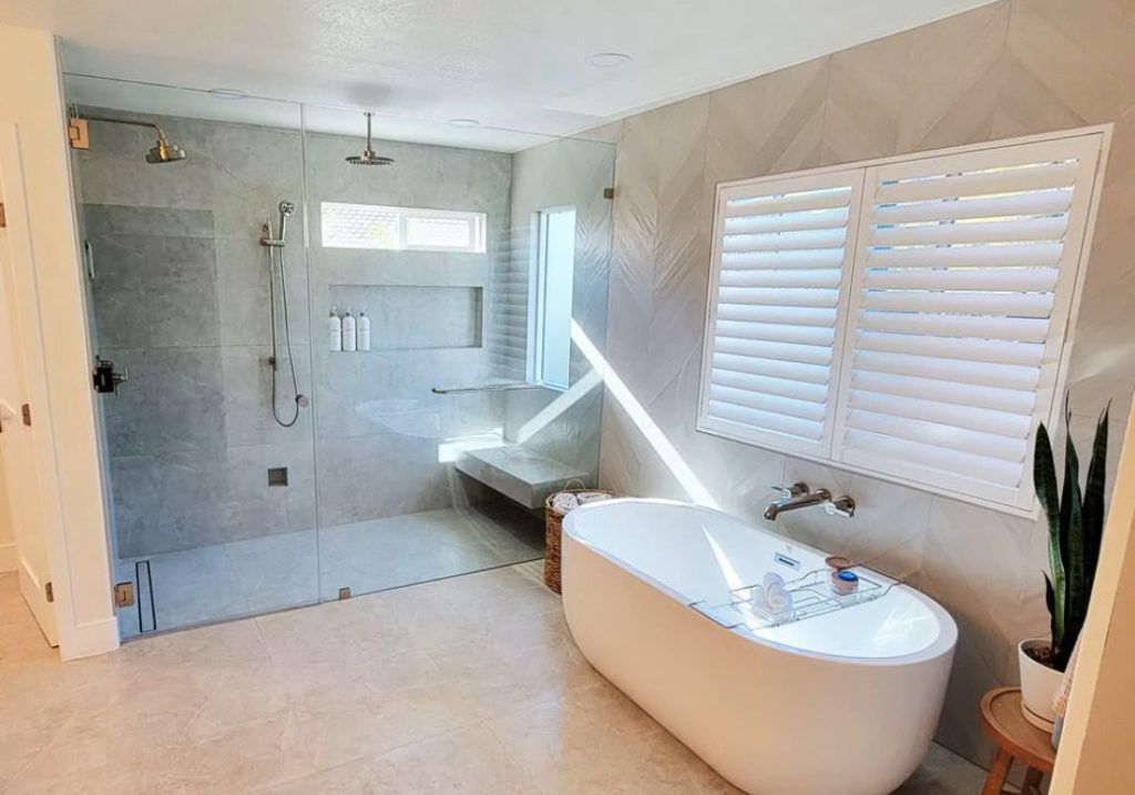 Modern bathroom with a glass-enclosed shower, freestanding bathtub, and a window with shutters.