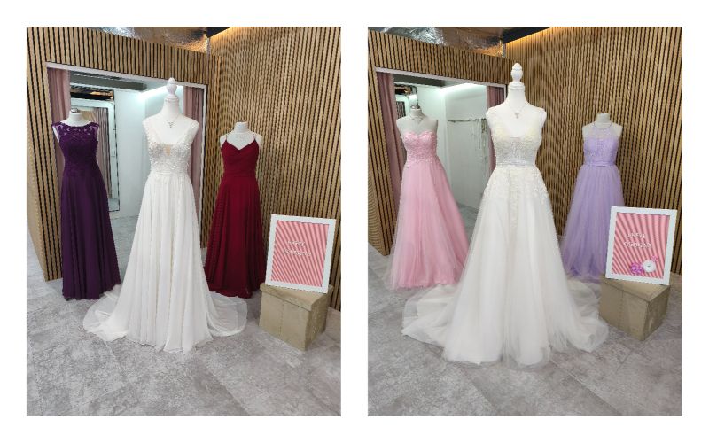 Drei Schaufensterpuppen in Abendkleidern, ein rosa Stuhl und ein Spiegel in einer Boutique.
