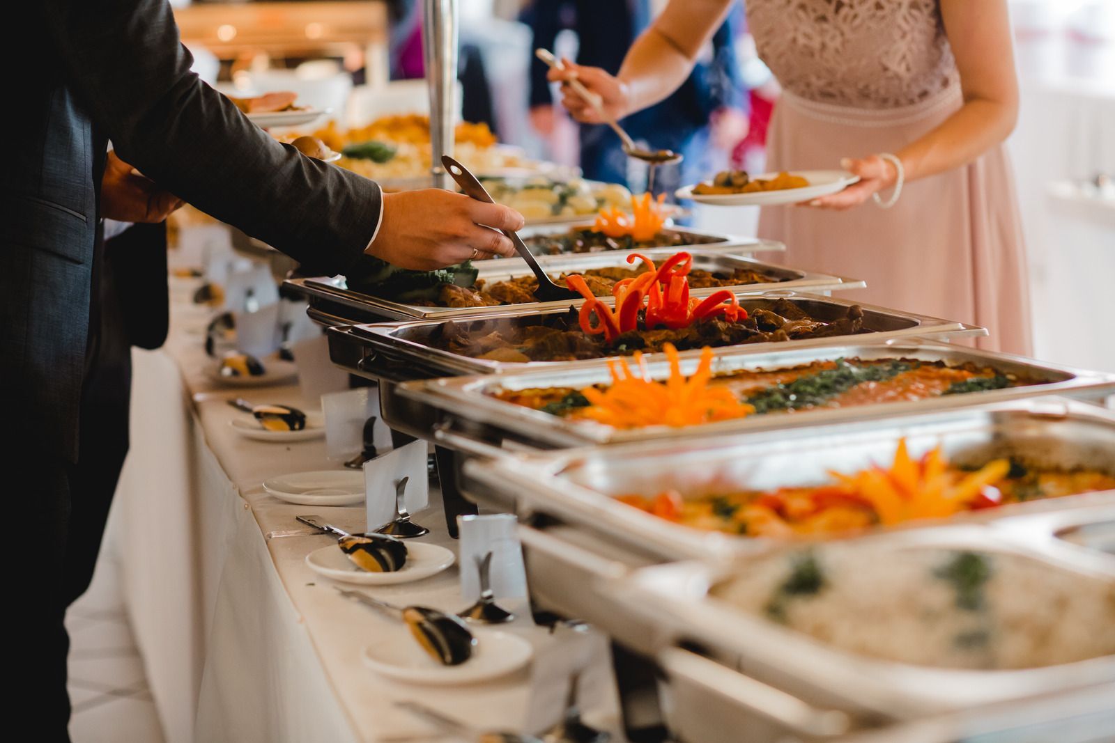A woman is taking a plate of food from a buffet line at a wedding reception.