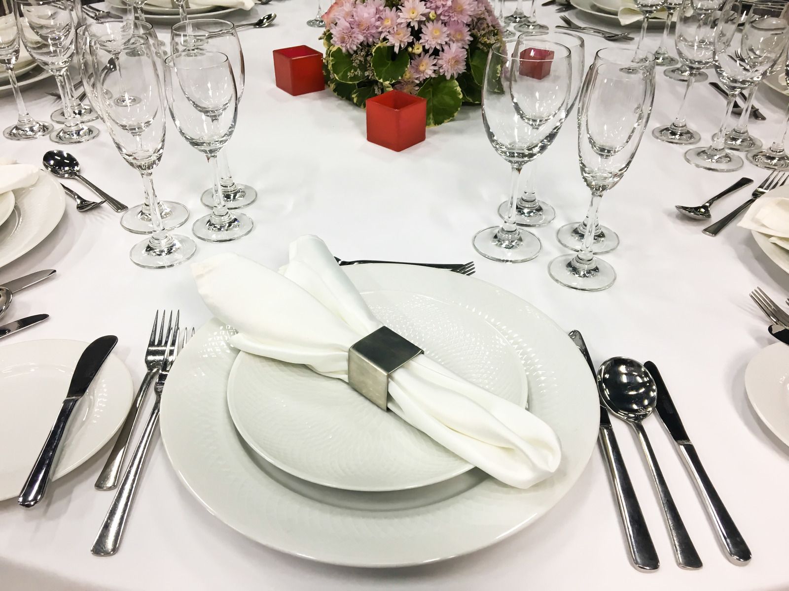 A table set for a wedding reception with plates , utensils , and wine glasses.