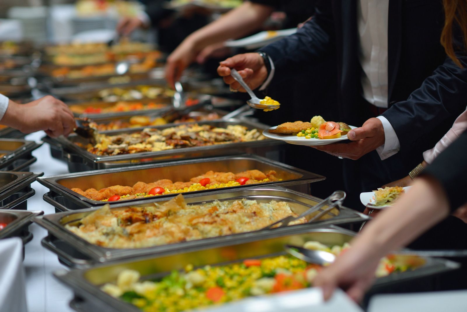 A group of people are taking food from a buffet line.