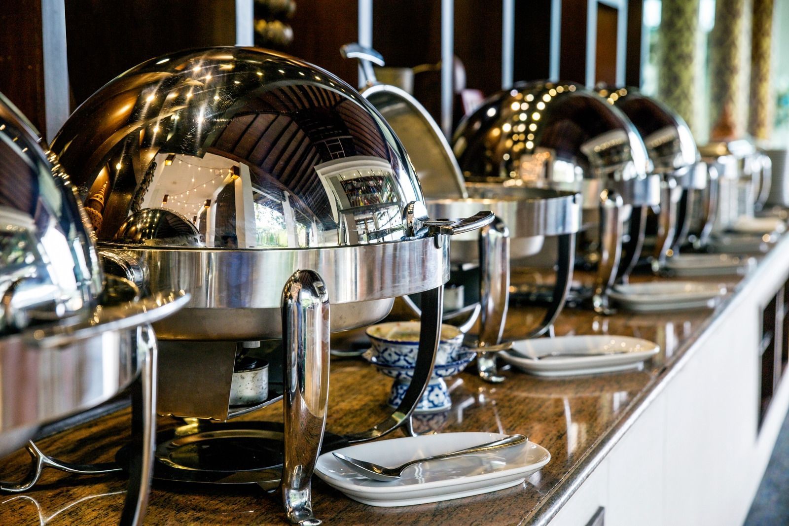 A row of stainless steel buffet servers lined up on a counter.