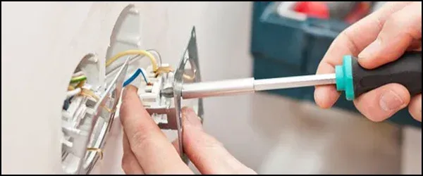 A person is fixing a light switch with a screwdriver.