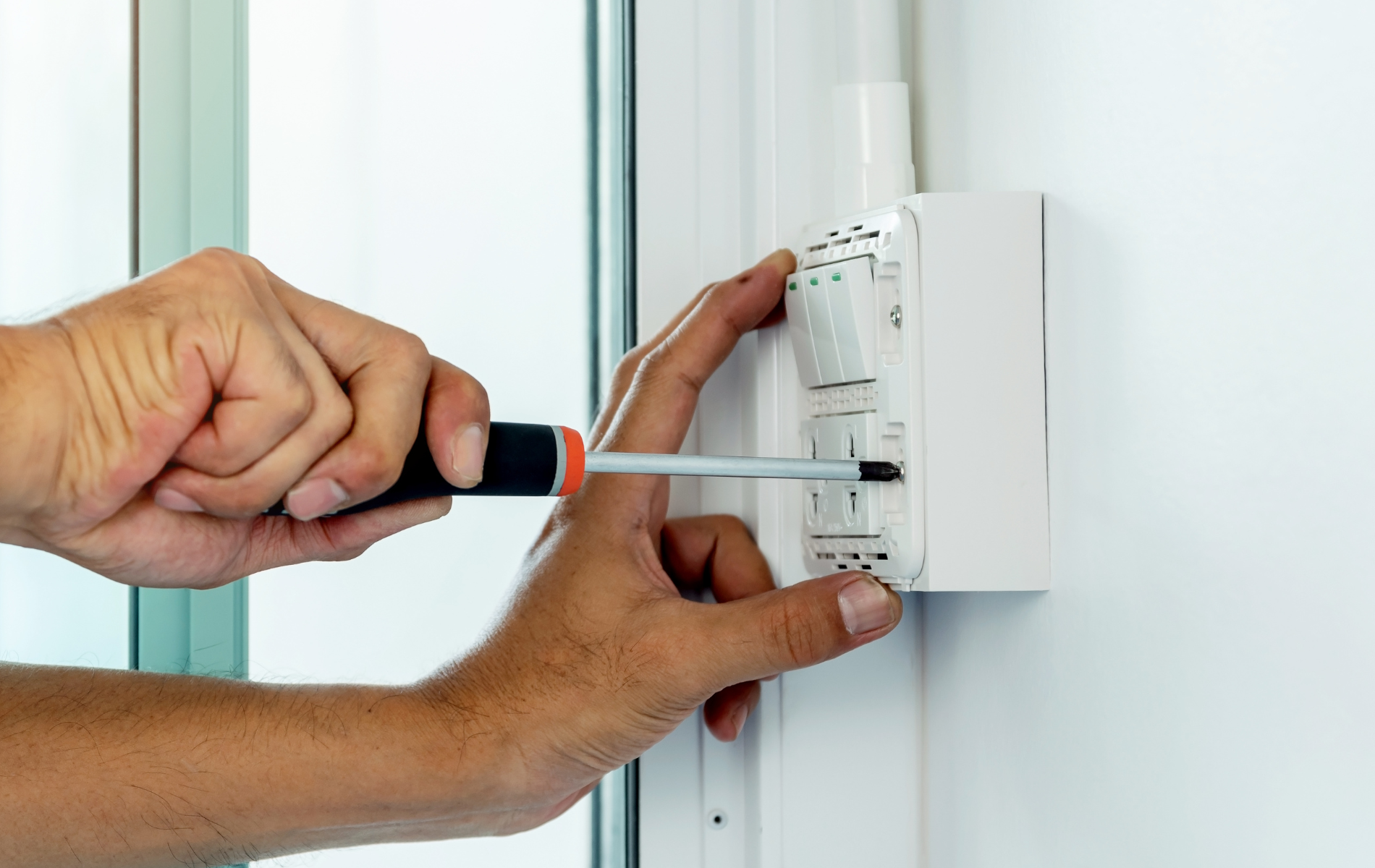 A person is using a screwdriver to fix a light switch.