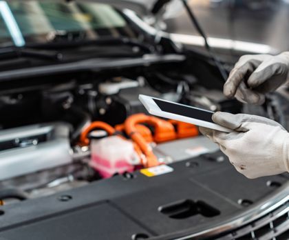 A person is holding a tablet in front of a car engine.