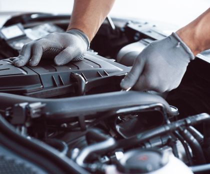 A person wearing gloves is working on the engine of a car.