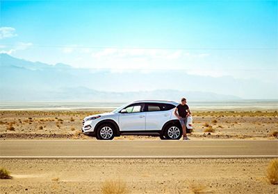 A man is standing next to a white suv on the side of a desert road.