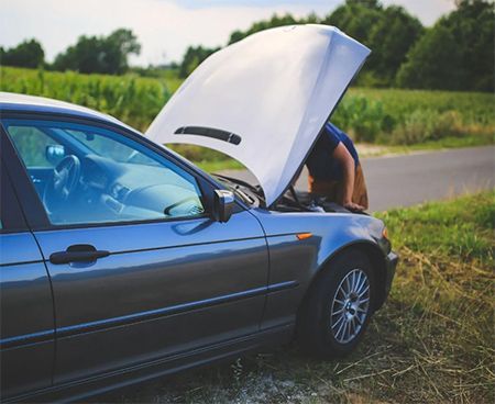 A man is looking under the hood of his broken down car.