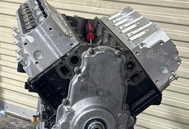 A partially assembled V8 engine block with silver aluminum cylinder heads and a timing cover against a slatted background.