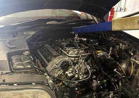 Car engine being lifted out of a black vehicle's open hood using a hoist in a garage.