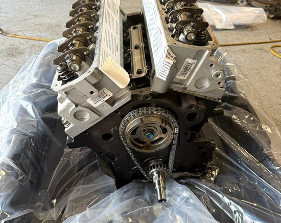 Engine block with cylinder heads, timing chain visible. Black engine components on plastic sheeting.