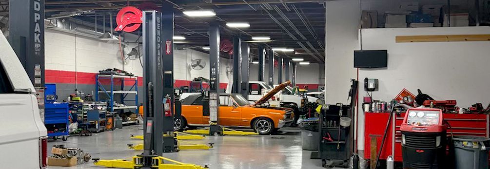 An auto repair shop with an orange car on a lift. Tools and equipment are scattered about.
