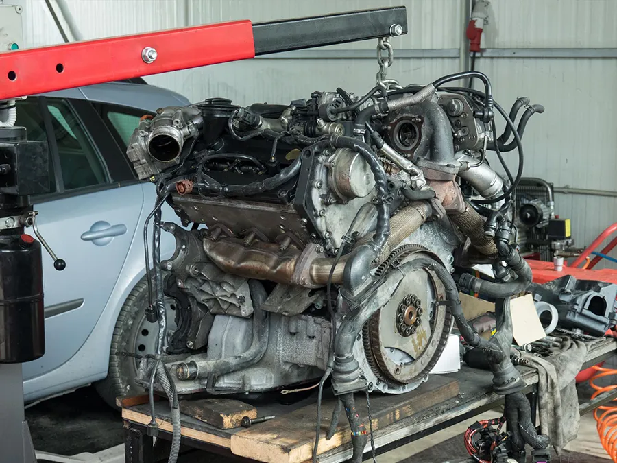 A car engine is sitting on top of a wooden table in a garage.