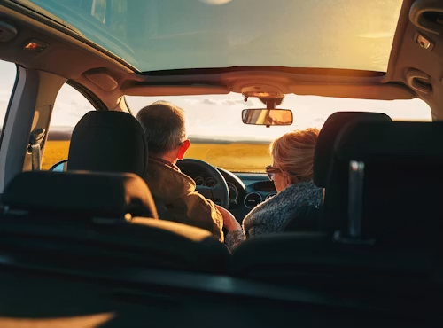 Two people in a car driving at sunset, seen from the back seat