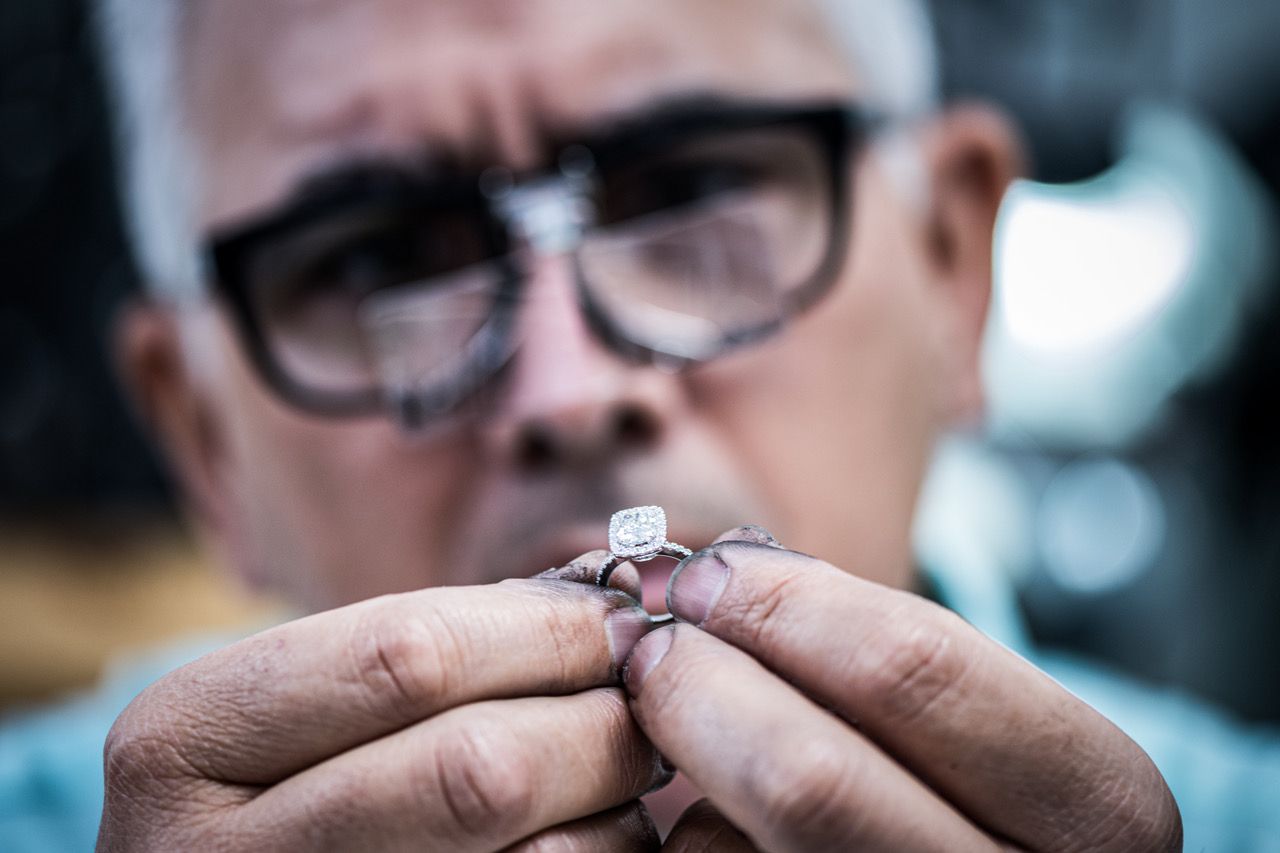 A man wearing glasses is holding a diamond ring in his hands.
