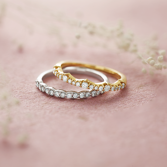 Two wedding rings are sitting on top of each other on a pink surface.