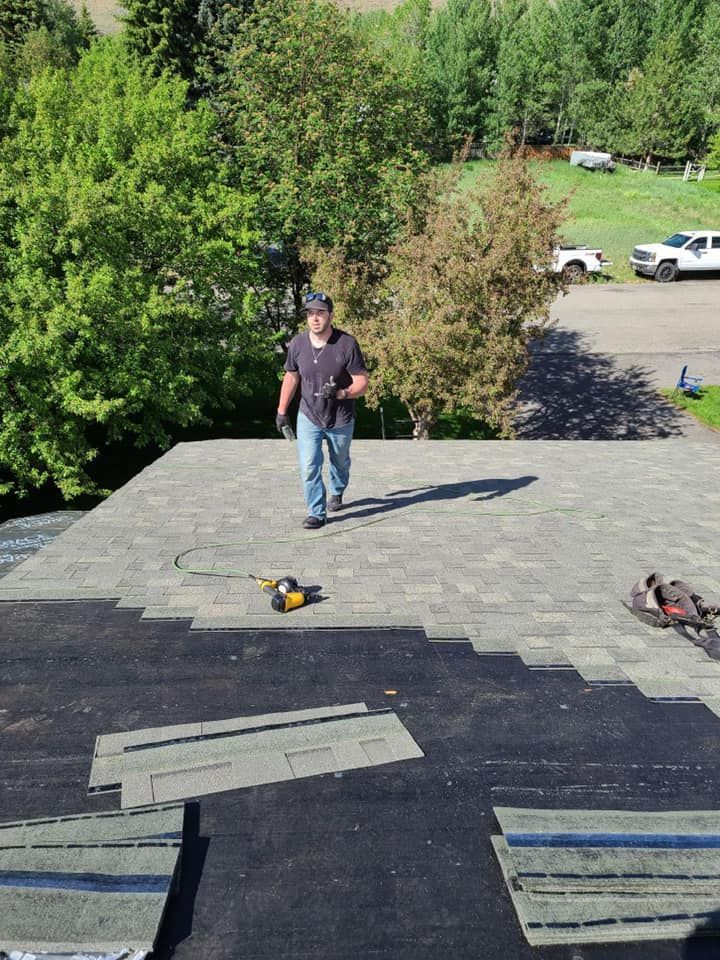 A man is standing on top of a roof with a drill.