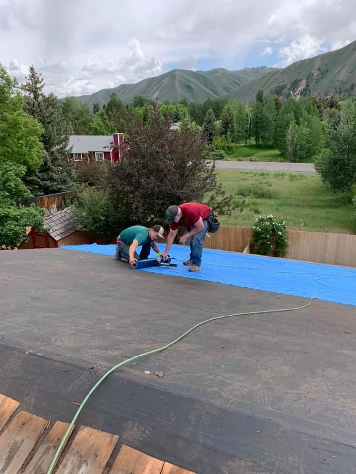 Two men are working on a roof with mountains in the background.