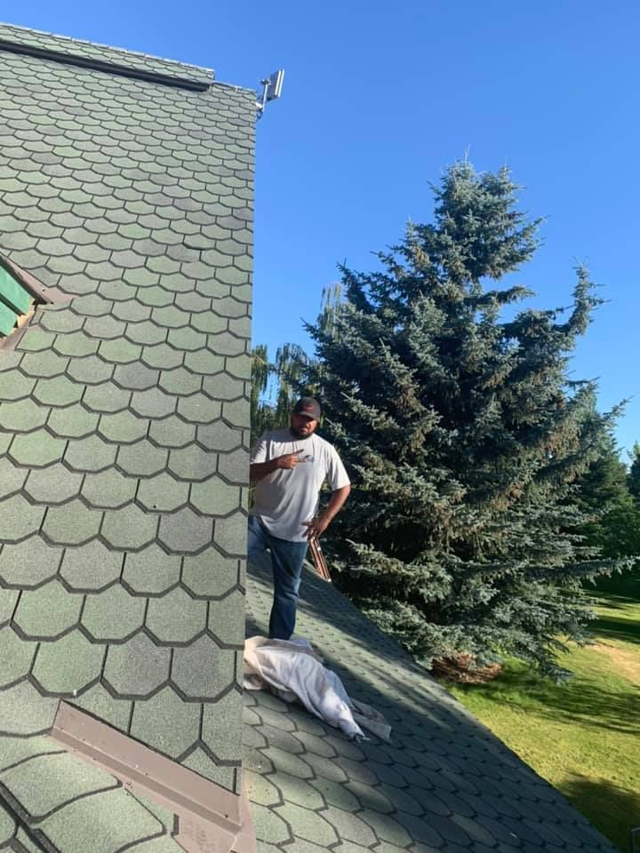 A man is standing on the roof of a house next to a tree.